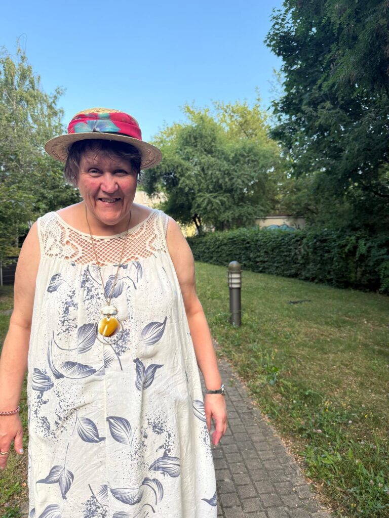 Eine Frau steht in einem Sommerkleid mit einem Sommerhut auf einem Weg im Grünen.