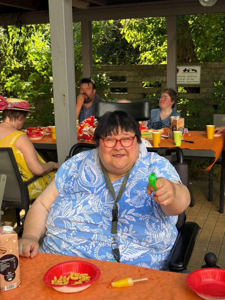 Eine Frau sitzt an einem Tisch und hält lachend eine Wasserpistole in die Kamera.
