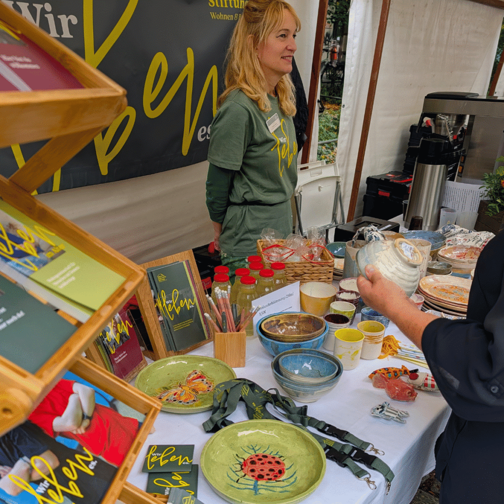 Eine Mitarbeiter in der Albert Schweitzer Stiftung Wohnen und Betreuen steht hinter dem Stand. Sie trägt ein grünes T-Shirts mit der Aufschrift